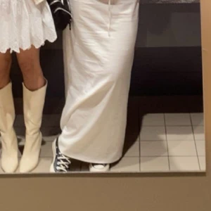 Vit långkjol med knytband - Säljer en stilren vit långkjol med knytband i midjan och slits på ena sidan. Kjolen har en enkel design och är perfekt för en avslappnad look. Den är gjord i ett lätt material som ger en skön känsla.