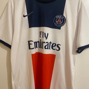 Vit PSG fotbollströja med Ibrahimović 10 - Säljer en vit PSG fotbollströja från Nike med Ibrahimovićs namn och nummer 10 på ryggen. Tröjan har korta ärmar och klubbens emblem på bröstet. Perfekt för fans av Paris Saint-Germain och Zlatan Ibrahimović! 🏟️