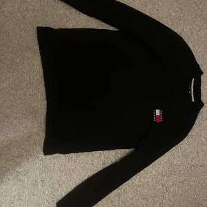 Svart långärmad tröja från Tommy Jeans - Säljer en stilren svart långärmad tröja från Tommy Jeans. Tröjan har en klassisk design med en liten logotyp på bröstet. Perfekt för en avslappnad och trendig look.
