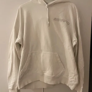 Vit hoodie från Axel Arigato - Säljer en stilren vit hoodie från Axel Arigato med en stor grafisk design på ryggen. Tröjan har en känguruficka och justerbar huva med dragsko. Perfekt för en avslappnad stil.