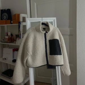 Beigevit teddyjacka med svart ficka - Säljer en mysig beige teddyjacka från gina, den är i väldigt fint skick fast än den är använd och är ett super fint plagg till våren men ett svartlinne under eller med en svart långklänning 🖤