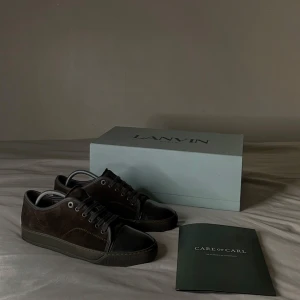 Bruna sneakers från Lanvin - Otroligt snygga bruna sneakers från Lanvin med en stilren modell. Skorna har snörning och är tillverkade i mocka med en glansig tå framsida i skinn. Perfekta för en trendig look. Kvitto samt Orderbekräftlse ingår, inskaffadde från Care of Carl, storlek 41 men kan även användas i någorlunda större storlek. Mvh 