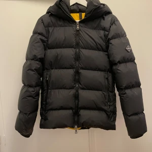 jacka från J.Lindeberg - Snygg svart dunjacka från J.Lindeberg med huva och dragkedja. Jackan har en quiltad design och en logotyp på ärmen. Perfekt för kyliga dagar köpt för 4000 men säljer den nu för 2200 går att diskutera kond 8/10 storlek XS men sitter som S