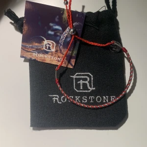 Rött och vitt armband från Rockstone - Snyggt armband från Rockstone i rött och vitt med en liten metallbricka. Armbandet har en enkel och stilren design med en justerbar knut för perfekt passform. Perfekt accessoar för att ge din outfit en färgklick.