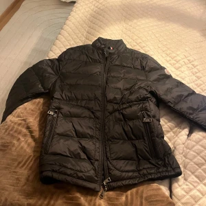 Svart dunjacka från Moncler - Säljer en snygg svart dunjacka från Moncler. Jackan har en dragkedja framtill och två fickor med dragkedjor. Den är quiltad och har en hög krage för extra värme. Perfekt för kyliga dagar! Modellen heter Longue Saison storlek är 2 som motsvarar 38. Kvitto minns ej men dust bag finns 