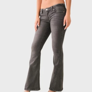 Grå bootcut jeans - Snygga grå bootcut jeans med låg midja och klassisk femficksdesign. Jeansen har dekorativa sömmar och knappar på bakfickorna som ger en unik touch. Perfekta för en avslappnad stil. Råkade köpa försmå, och har inte hunnit lämna tbx. Dom är aldrig använda ute, endast testade. Kan vara intressant o byta emot en större storlek (24)  i valfri färg