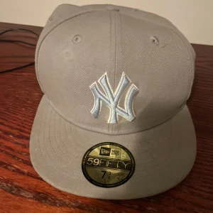 Grå/Blå keps från New Era - Snygg grå keps från New Era med broderad logga framtill och på sidan. Storlek 7 3/4