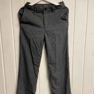 Grå randiga kostymbyxor - Snygga grå kostymbyxor med diskreta ränder. De har en klassisk design med knappar och dragkedja framtill. 