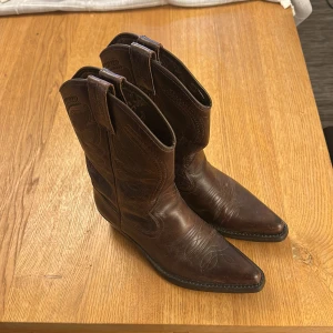 Bruna Texas boots i skinn - Snygga bruna Texas boots i skinn med dekorativa broderier. De har en spetsig tå och en låg klack, vilket ger dem en klassisk western-look. Perfekta för att ge din outfit en cool touch. Använda en gång  