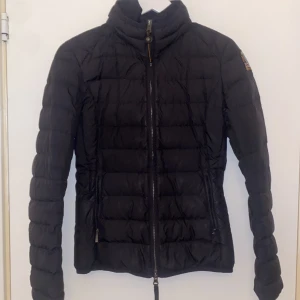 Svart dunjacka från Parajumpers - Säljer en svart dunjacka från Parajumpers i superlätt material. Jackan har en dragkedja framtill och ett broderat märke på ärmen. Perfekt för kyliga dagar med stil. 🖤