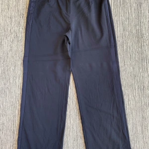 Marinblå byxor från Newhouse - Snygga marinblå byxor från Newhouse med en klassisk design. Byxorna har en rak passform och är tillverkade i ett mjukt material som ger en bekväm känsla. Perfekta för en stilren look. Marinblåa vida kostymbyxor i strl 40 från Newhouse.  Byxorna har revär i sidorna.  Sparsamt använda och i fint begagnat skick.  Mått Midjan: ca 41 cm Längd från grenen och ner: ca 73 cm  69% viskos, 28% ull och 3% elastan   Kommer från ett djur och rökfritt hem. 