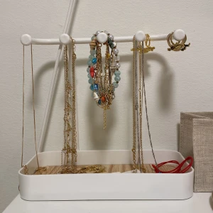 Smyckesställ i vit metall och trä - Praktiskt smyckesställ i vit metall med en bas av träimitation. Perfekt för att organisera halsband, armband och ringar. Stället har flera krokar för enkel upphängning och en stabil bas för säker förvaring.