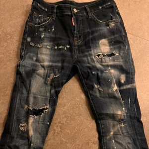 Dsquared2 jeans - Snygga mörkblå jeans från Dsquared2 med coola slitningar och en unik 'Ciao Bella' patch på baksidan. Jeansen har en klassisk femficksdesign och en modern look med slitna detaljer. Perfekta för en trendig stil!