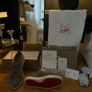 Grå sneakers från Christian Louboutin - Snygga grå sneakers från Christian Louboutin med den ikoniska röda sulan. Skorna har snörning och är tillverkade i mocka, vilket ger en lyxig känsla. Perfekta för den som vill ha stil och komfort i ett. Dom är lite smutsiga som nu ser på första bilden men annars är dom i väldigt bra skick kan gå ner i pris vid snabb affär 