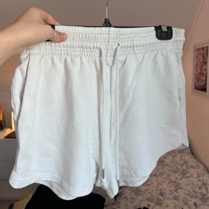 Vita mjukisshorts - Säljer ett par vita mjukisshorts från H&M med elastisk midja och snören fram. Perfekta för en avslappnad stil. De har en enkel design med fickor på sidorna. Finns en liten fläck som syns på näst sista bilden. Önskar du veta exakta mått? Tveka inte att höra av dig!