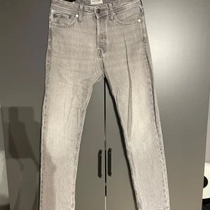 Jack&Jones jeans - Snygga grå jeans från Jack & Jones med en avslappnad passform, med knappgylf. Hör av er vid frågor, pris ej hugget i sten.                                 Modellen är Chris                         Storleken är W27 L30