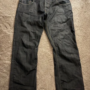 Mörk blåa jeans från G-Star - Snygga mörk blåa jeansbyxor från G-Star med klassisk design och fem fickor. Byxorna har en mörk tvätt och är perfekta för en stilren look. Märkesdetaljer syns på baksidan med en läderpatch.