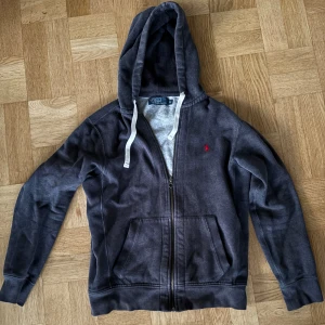 Mörkgrå hoodie från Polo Ralph Lauren - Säljer en snygg mörkgrå hoodie från Polo Ralph Lauren med dragkedja och vit snörning i huvan. 