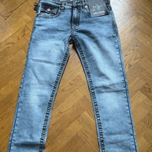 Blå jeans från True Religion - Snygga blå jeans från True Religion med klassisk femficksdesign och kontrastsömmar. De har en straight passform och är tillverkade i slitstarkt denim. Perfekta för en avslappnad stil.