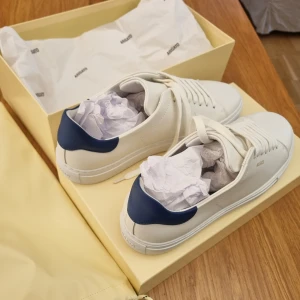 Vita sneakers från Axel Arigato - Feta vita sneakers från Axel Arigato som har en stilren design och blå detalj vid hälen, perfekt inför sommaren🤗 Skorna har klassisk snörning och är perfekta för en minimalistisk look. Levereras i originalförpackning och med dustbag. Sprillans nya endast prövade en gång. Säljs pga de inte passar mig. NY PRIS 2600!