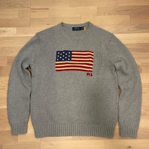 Ralph Lauren USA flagga - Säljer en stilren grå stickad tröja från Ralph Lauren med den ikoniska amerikanska flaggan. Tröjan är i storlek M men passar mera S! Jätte populär tröja just nu som passar till allt! Skick 10/10