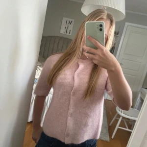 Rosa stickad kofta med knappar - Säljer en söt rosa stickad kofta med korta ärmar och knappar framtill. Perfekt för en mysig och stilren look. Koftan har en ribbad struktur som ger en fin textur. Storlek 158/164