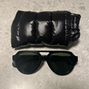 Moncler solglasögon - Snygga svarta solglasögon från Moncler med en modern design. Tillverkade i Italien, de har en robust ram och mörka linser. Perfekta för en stilren outfit. Hör av er vid frågor!