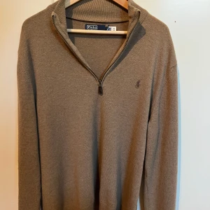 Polo Ralph Lauren Beige Quarter Zip - Säljer en stilren beige tröja från Polo Ralph Lauren med dragkedja och broderad logga på bröstet. Perfekt för en avslappnad men ändå elegant look. Tröjan har långa ärmar och en ribbad krage.