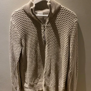 Beige stickad tröja från Selected Homme - Säljer en snygg beige stickad tröja från Selected Homme. Tröjan har en dragkedja framtill och en ribbad krage. Perfekt för kyligare dagar med sin stilrena design och bekväma passform.