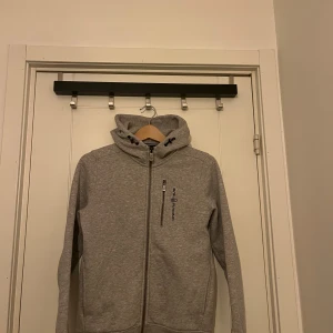 Grå huvtröja från Sail Racing - Säljer en stilren grå huvtröja från Sail Racing. Hör av dig vid funderingar!