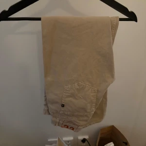 Beigea donup byxor - Snygga beige kinos med klassisk femficksdesign. Byxorna har en normal passform och är perfekta för en avslappnad stil. De är tillverkade i ett slitstarkt material och har en knappgylf framtill. Skulle mer säga att det är strl 31 eller 32 än 33.