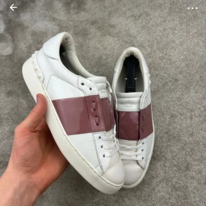 Valentino Garavani sneakers med rosa detalj - OBS bilderna är från han jag köpte av! Snygga vita sneakers från Valentino Garavani med en bred, glansig rosa rem över snörningen. Skorna har en klassisk design med rund tå och en bekväm sula. Perfekta för att ge din outfit en lyxig touch. 2200kr vid snabba köp! Köp gärna på Vinted istället för här namn: elvira5234