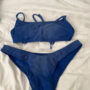 Blå bikini med knytband - Snygg blå bikini med enkel design och knytband på toppen. Perfekt för en dag på stranden eller vid poolen. Både överdel och underdel har en stilren look.