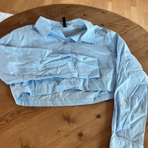 Ljusblå croppad skjorta - Säljer en ljusblå croppad skjorta med långa ärmar och knappar framtill. . Skjortan har en klassisk krage och är tillverkad i ett lätt material.