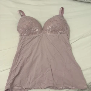 Ljuslila spetsdetaljerad linneklänning - Säljer en ljuslila linneklänning med vackra spetsdetaljer på bysten. Klänningen har justerbara axelband och en mjuk, följsam passform. Perfekt som ett elegant underplagg. Jag skulle säga att det är ungefär C/D kupa.