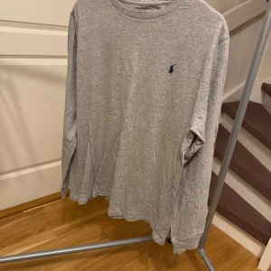 Grå långärmad tröja från Ralph Lauren - Säljer en stilren grå långärmad tröja från Ralph Lauren med det klassiska broderade logotypen på bröstet. Perfekt för en avslappnad och snygg look. Tröjan är i mjukt bomullsmaterial och har en normal passform. Storlek: L Nypris: 699kr