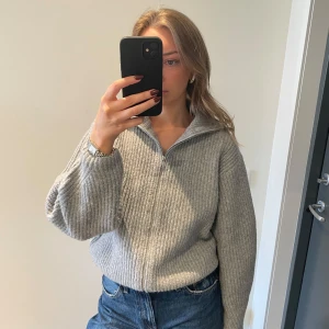 Grå stickad tröja från BikBok - Säljer en mysig grå stickad tröja från BikBok med dragkedja framtill. Tröjan har en hög krage och långa ärmar, perfekt för kyliga dagar. Den ribbade strukturen ger en stilren look. Passar bra till jeans eller kjol.