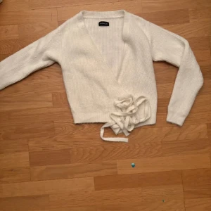 Vit omlottkofta från Gina Tricot - Säljer en mysig vit omlottkofta från Gina Tricot. Koftan är stickad med långa ärmar och har ett knytband i midjan. Perfekt för kyliga dagar!