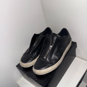 Svarta sneakers med dragkedja - Snygga svarta skor från Axel Arigato skinn med dragkedja fram till. De har en vit sula. Använda ganska mycket. Skulle säga att det är acceptabelt skick lite slitna. Säljs ej i butik. Tyvärr inte original boxen. Skorna är storlek 41 men skulle säga att det är storlek 42. Diskutera om priset i chatten 
