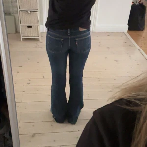 Blå bootcut jeans Levis  - Snygga blå bootcut jeans från Levis. De har en klassisk femficksdesign och är perfekta för en avslappnad stil. Jeansen har en låg midja och är omsydda av dem som står på lappen på sista bilden. Säljer då de tyvärr är för små för mig. Slitna vid hälarna vilket syns på bild 3. Mått: 35 cm & 82 cm