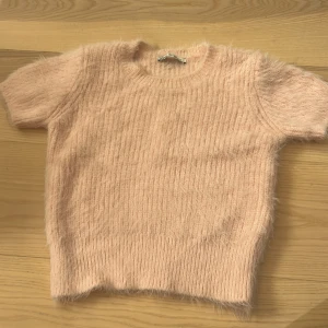 Ljusrosa fluffig tröja - Säljer en supermjuk och fluffig ljusrosa tröja med korta ärmar. Perfekt för en mysig dag hemma eller en avslappnad utflykt. Tröjan har en enkel design med rund hals och är gjord i ett material som känns som en dröm mot huden.