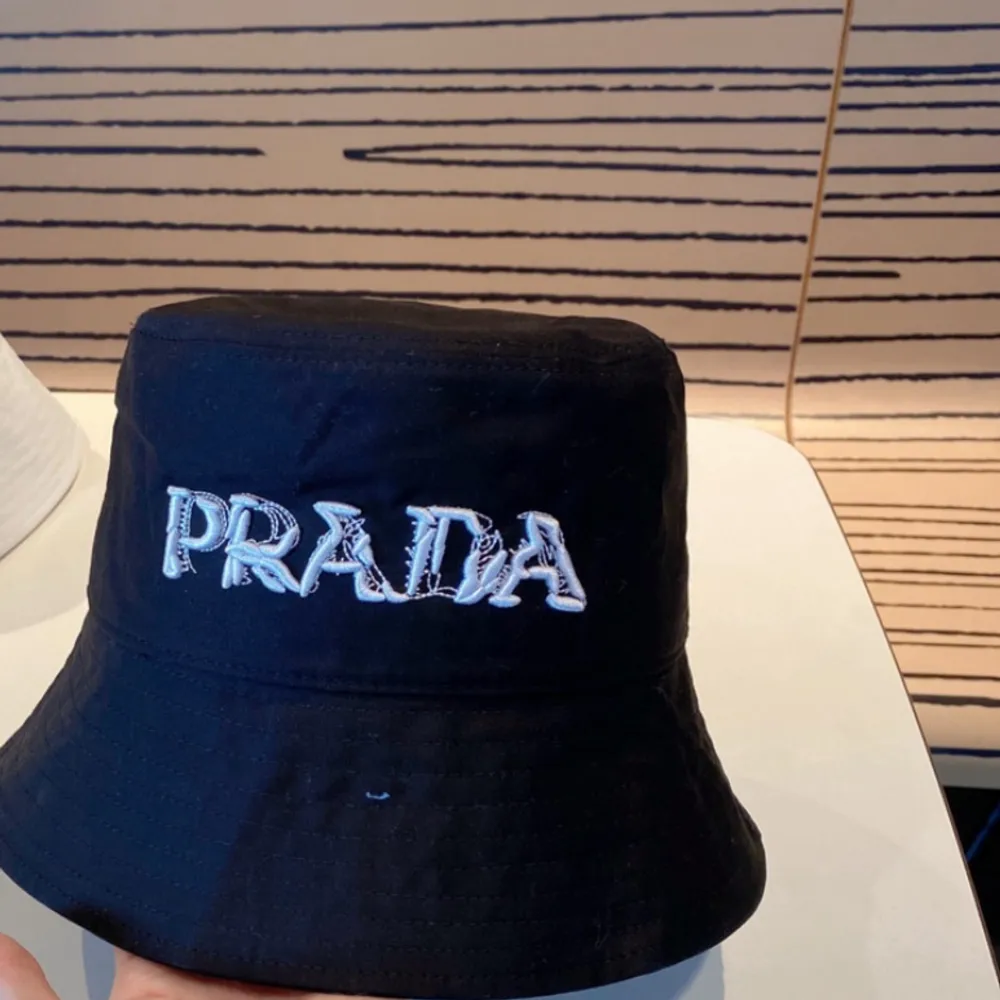 Snygg svart bucket hat från Prada med broderad logga i vitt framtill. Perfekt för att ge din outfit en stilren touch. Hatten har en klassisk form och är tillverkad i ett bekvämt material. Riktigt stil ren Prada Hat som passar till alla outfits skriv för funderingar 🤔 tveka inte ens att skiva 😉 parfeckt in för våren/somamren😊. Asusteet.