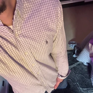 Rutig skjorta från Ralph Lauren - Säljer en stilren rutig skjorta från Ralph Lauren i bomull. Skjortan har en klassisk krage och knappar framtill. Den är vit med ett diskret rutmönster i grått och har en broderad logotyp på bröstet. För mer bilder / frågor skriv ! 