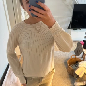 Beige stickad tröja från Daisy - Säljer en stilren beige stickad tröja från Daisy. Tröjan har ett ribbat mönster upptill och långa ärmar. Perfekt för en avslappnad och elegant look.