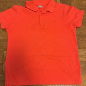  pikétröja - Säljer en snygg orange pikétröja från Nukutavake/ mayoral. Tröjan har en klassisk krage och knappar framtill. Perfekt för en avslappnad stil.