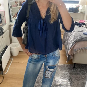 Blå blus med knytband - Säljer en stilren blå blus med v-ringning och knytband framtill. Blusen har trekvartsärmar och en luftig passform, perfekt för både vardag och lite finare tillfällen. Materialet är lätt och bekvämt.