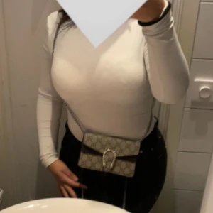 Gucci Dionysus axelväska - Säljer en stilren Gucci Dionysus axelväska i svart och beige med kedjerem. Väskan har ett ikoniskt spänne och är tillverkad i patenterat skinn. Perfekt för att ge en lyxig touch till din outfit. Köpte den för 10.841kr då den inte var på REA som den är nu, och har haft den i snart ett halvt år och har tröttnat på den har använt den mycket men den har inga skador och fel som ni ser på den senaste gången jag hade på mig den så jag säljer den för nästan halva priset. 🤍priset kan absolut diskuteras.