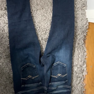 Mörkblå jeans från Replay - Snygga mörkblå jeans från Replay med en klassisk femficksdesign. De har en knappgylf och bälteshällor, vilket gör dem perfekta för en avslappnad stil. Jeansen har en lätt tvättad look som ger dem en cool edge.