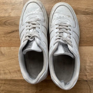 Vita sneakers - Säljer ett par vita sneakers med klassisk design och snörning. Skorna har en rund tå och är perfekta för en avslappnad stil. De har en enkel och stilren look som passar till det mesta.