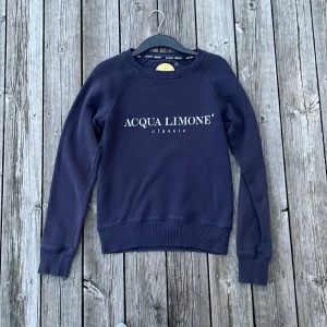 Mörkblå sweatshirt från Acqua Limone - Säljer en stilren mörkblå sweatshirt från Acqua Limone med tryck på både fram- och baksidan. Tröjan har långa ärmar och ribbade muddar vid ärmslut och nederkant. Perfekt för en avslappnad och enkel stil. Passar jättebra ihop med ett par linnebyxor och kan inte gå fel till sommaren. Storlek XS. Hör av dig vid funderingar. 